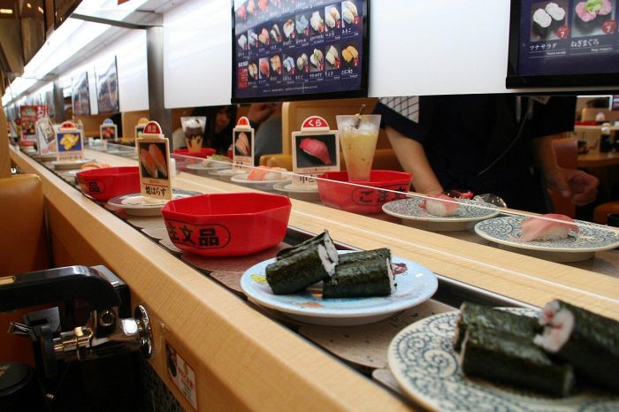 Ilustrasi khas Sushiro — piring sushi di atas ban berjalan